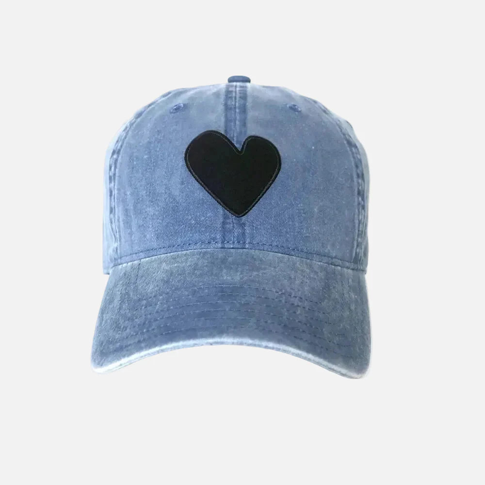 The Kerri Rosenthal Baseball Hat Heart Patch is a light blue denim cap with a large black heart embroidered on the front, displayed on a plain white background.