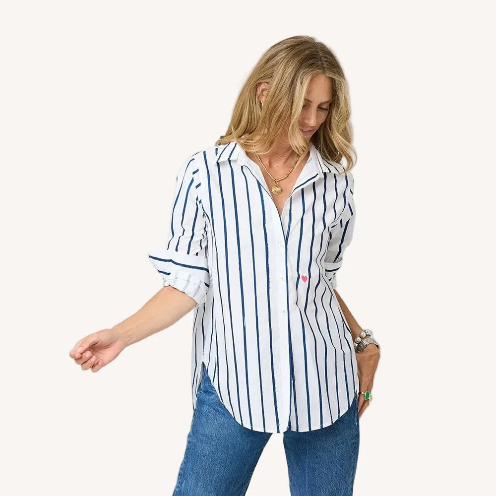 A woman models the Kerri Rosenthal Mia Mr Sharpie Stripe Shirt—white with navy blue stripes—paired with blue jeans and layered necklaces, standing with one arm slightly raised against a neutral background.