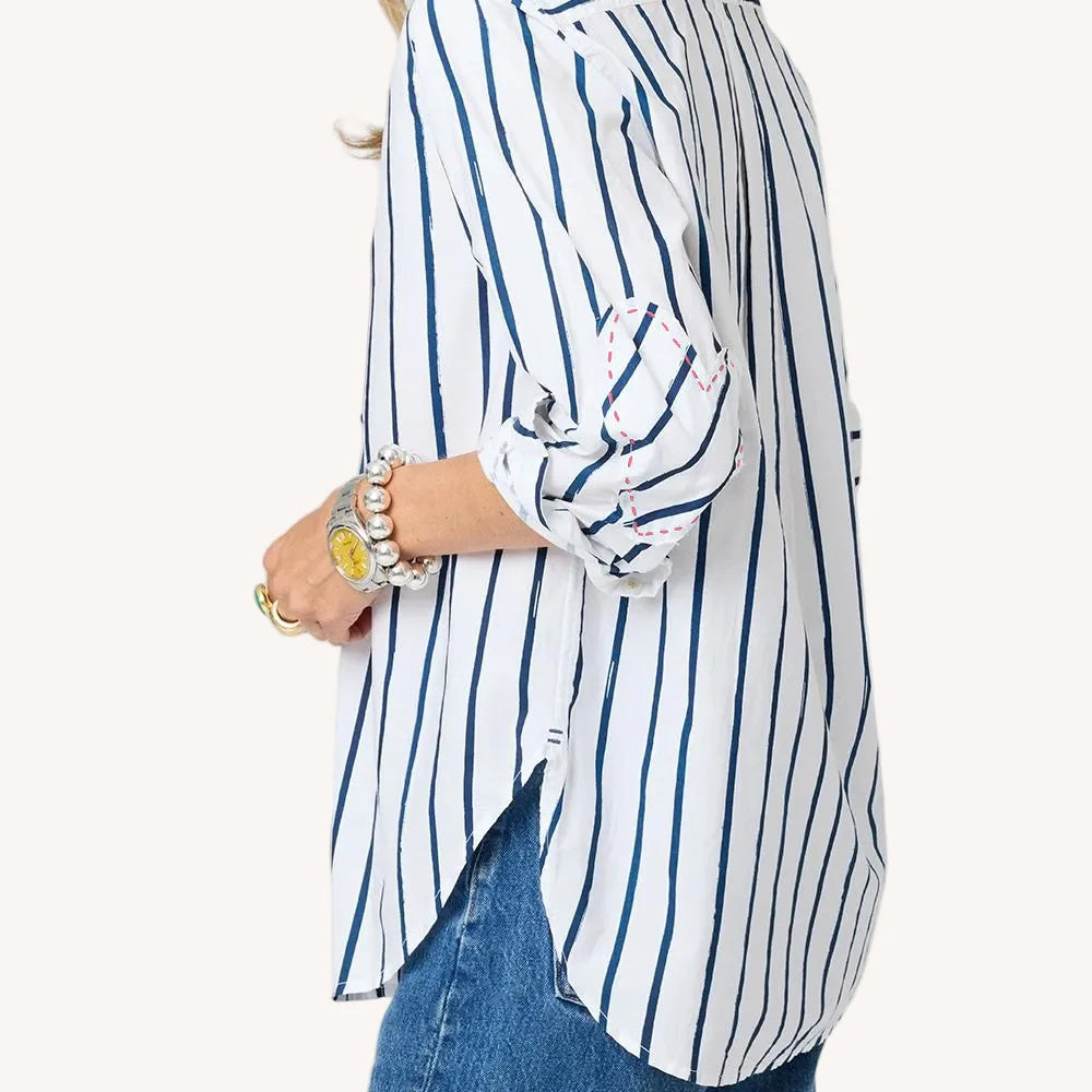 A woman wears the Kerri Rosenthal Mia Mr Sharpie Stripe Shirt—white with vertical blue stripes and rolled sleeves—paired with blue jeans, chunky bracelets, and a ring. Only her upper body is visible from the side.