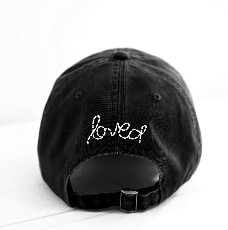 The Kerri Rosenthal Baseball Hat Heart Patch, shown from the back on a white background, features "loved" and a heart embroidered in white cursive above the adjustable strap—a stylish take on popular black baseball caps.
