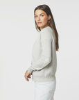 A woman with long brown hair wears a Willie Cashmere Cardigan by Kerri Rosenthal and white pants. She stands in profile, looking towards the camera with a neutral expression against a plain white background.