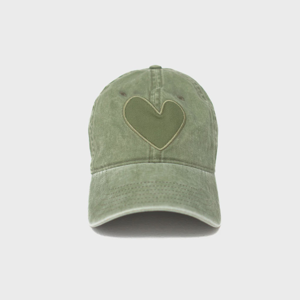 A green Imperfect Heart Hat crafted from stone-washed cotton, featuring a matching heart-shaped patch on the front. The cap boasts a curved brim and visible stitching details, all displayed on a plain white background. This stylish accessory is brought to you by Kerri Rosenthal.