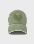 A green Imperfect Heart Hat crafted from stone-washed cotton, featuring a matching heart-shaped patch on the front. The cap boasts a curved brim and visible stitching details, all displayed on a plain white background. This stylish accessory is brought to you by Kerri Rosenthal.