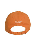 The back of the orange Texas Baseball Hat Heart Patch from Kerri Rosenthal's KR CAP-Sule Collection features "loved" embroidered in white and has an adjustable strap with a metal buckle.