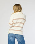 A person with long blonde hair is seen from behind wearing a Kerri Rosenthal Syd Sweater, featuring a cream cotton knit design with tan horizontal stripes, paired with blue jeans against a plain light gray background.