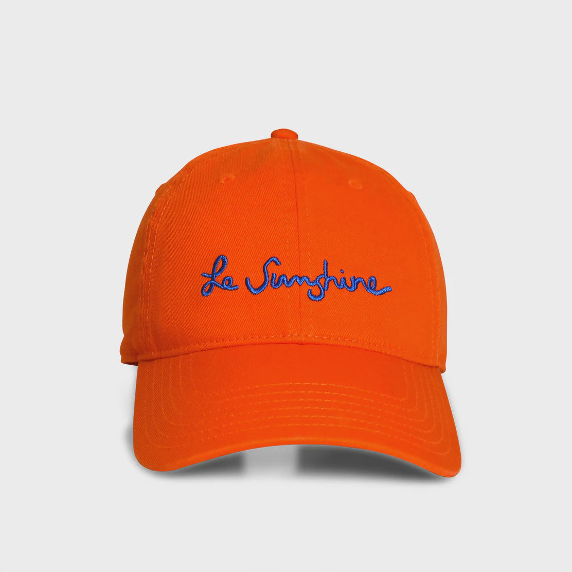 The KR Le Sunshine Hat by Kerri Rosenthal features &quot;Le Sunshine&quot; elegantly embroidered in blue on an Aperol orange cotton cap. Displayed against a plain white background, its vibrant hue stands out.