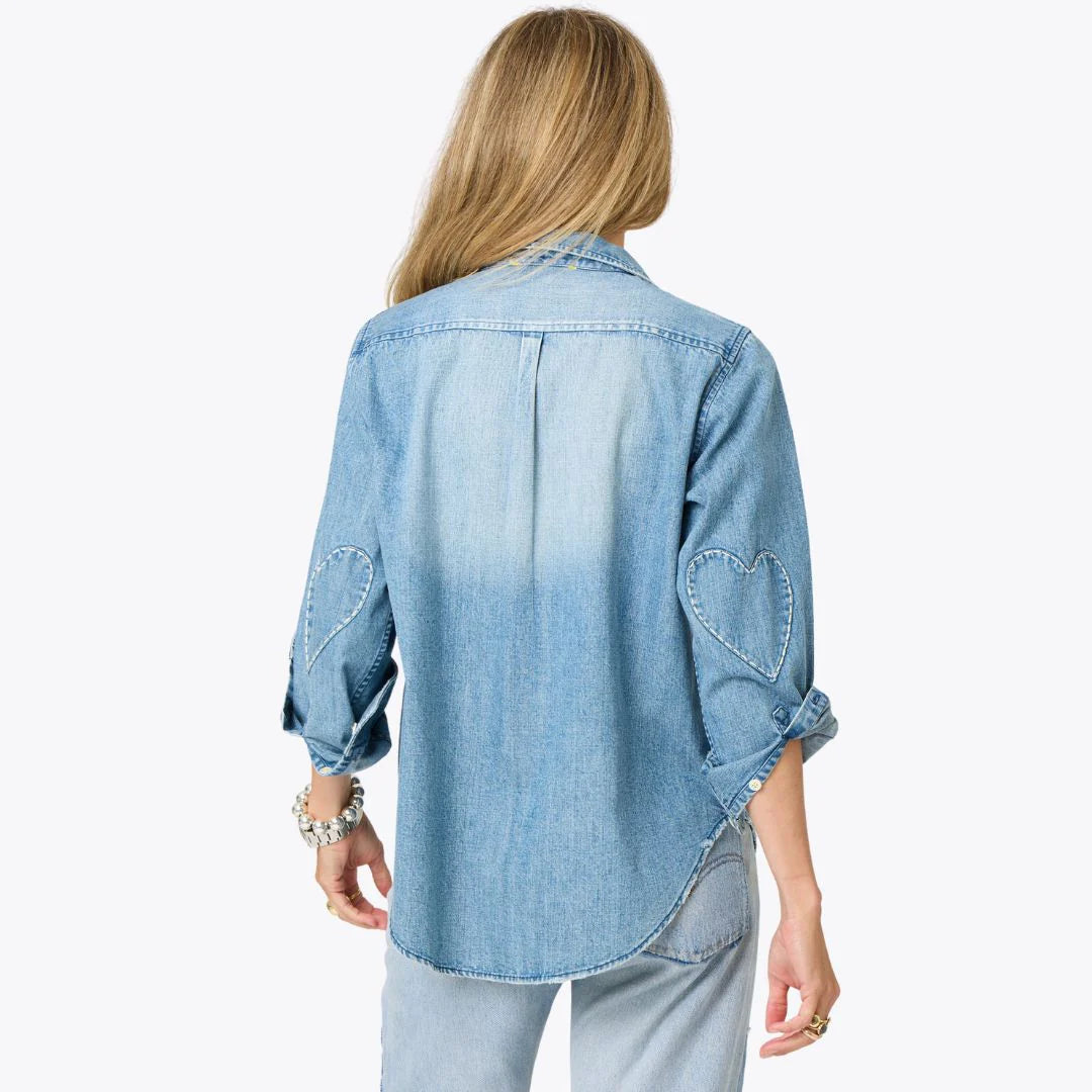 A woman with long blonde hair wears the Kerri Rosenthal Denim Shirt Lightweight, featuring rolled-up sleeves and embroidered heart elbow details, standing with her back to the camera against a plain background.