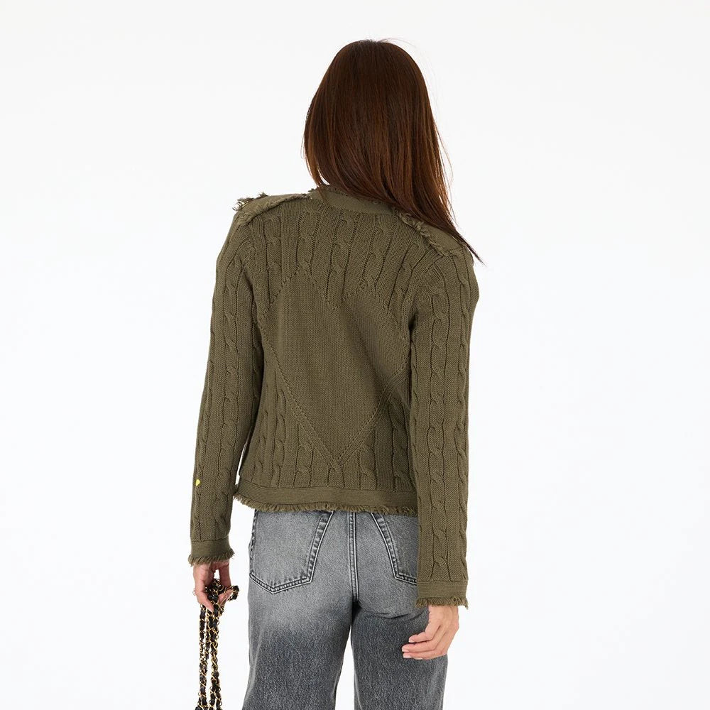 A person with straight brown hair stands with their back to the camera, wearing the Kerri Rosenthal Beau-Lero Fringe Cardigan in green and gray jeans. They hold a chain strap bag in their left hand against a plain white background.