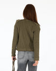 A person with straight brown hair stands with their back to the camera, wearing the Kerri Rosenthal Beau-Lero Fringe Cardigan in green and gray jeans. They hold a chain strap bag in their left hand against a plain white background.