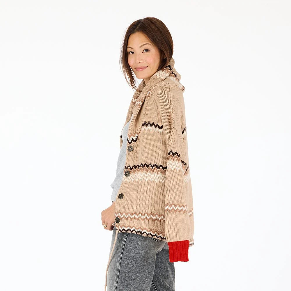 A woman stands sideways and smiles, wearing the Kerri Rosenthal Shawl Collar Ker-Isle Cardigan with black and white zigzags, a red cuff, light gray top, and gray jeans against a plain white background.