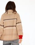 A person with long brown hair, seen from behind, wears the Kerri Rosenthal Shawl Collar Ker-Isle Cardigan in beige with black and cream zigzag stripes and red cuffs, paired with gray jeans, against a plain white background.