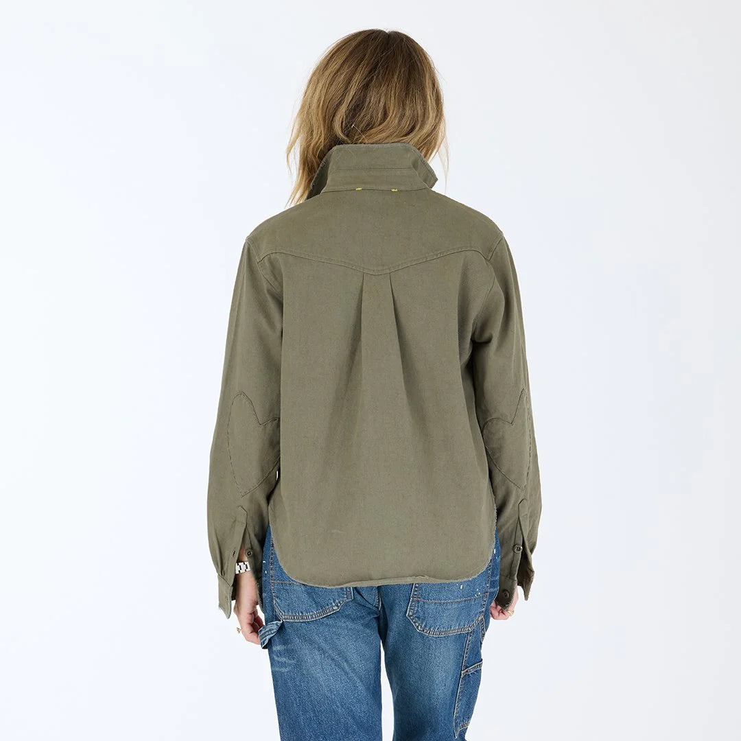 A person with long, light brown hair is seen from the back wearing the Kerri Rosenthal Pia Love Brigade Shirt and blue jeans, standing against a plain white background.