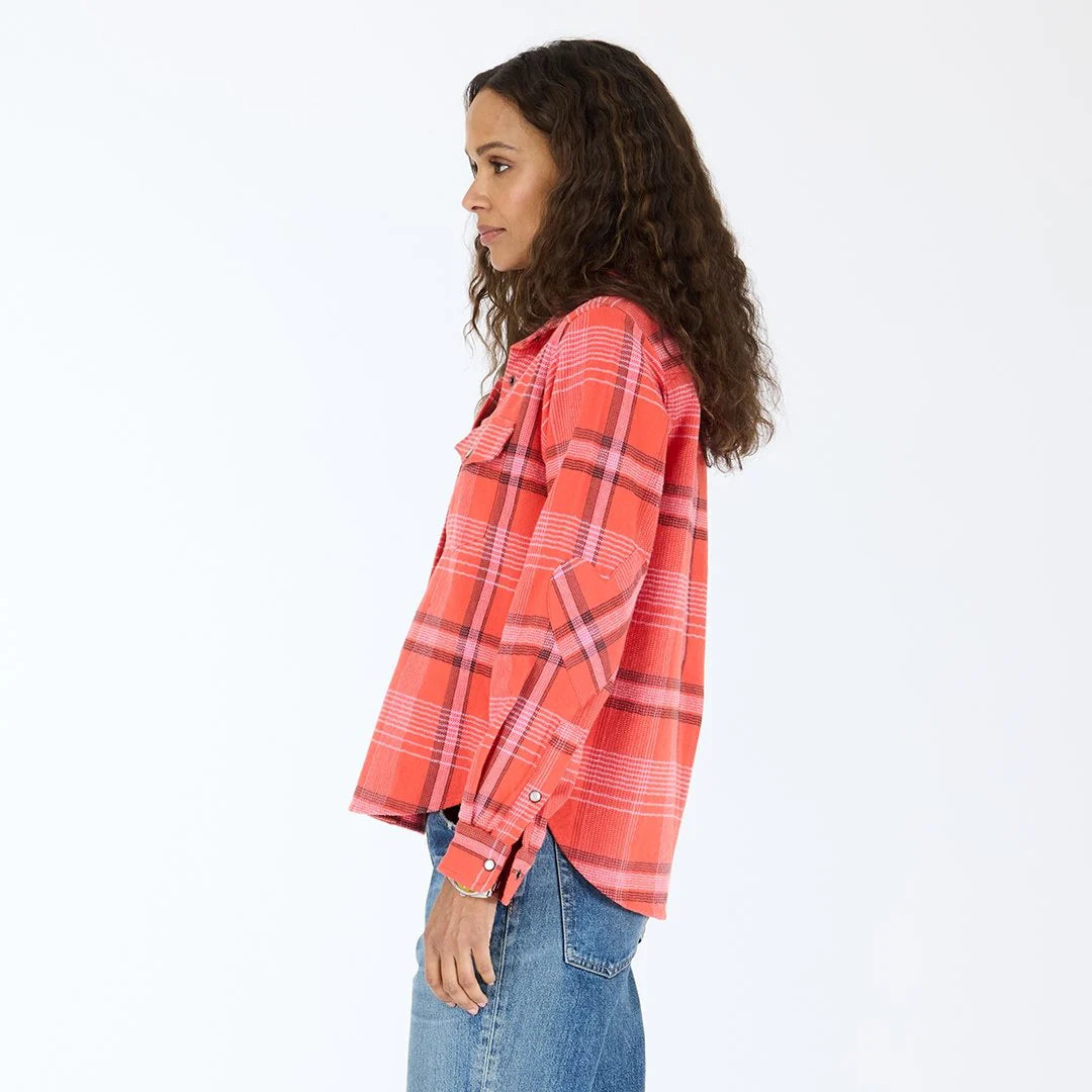 A woman with curly hair wears the Kerri Rosenthal Pia Western Flannel in red and pink, paired with blue jeans, standing in profile against a white background.