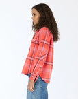 A woman with curly hair wears the Kerri Rosenthal Pia Western Flannel in red and pink, paired with blue jeans, standing in profile against a white background.