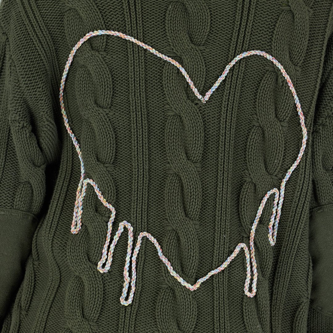 A close-up of the dark green Kerri Rosenthal Shawl Collar Helen Cardigan, featuring a drippy heart outlined in a multicolored braided cord, with the bottom of the heart appearing to melt downward.