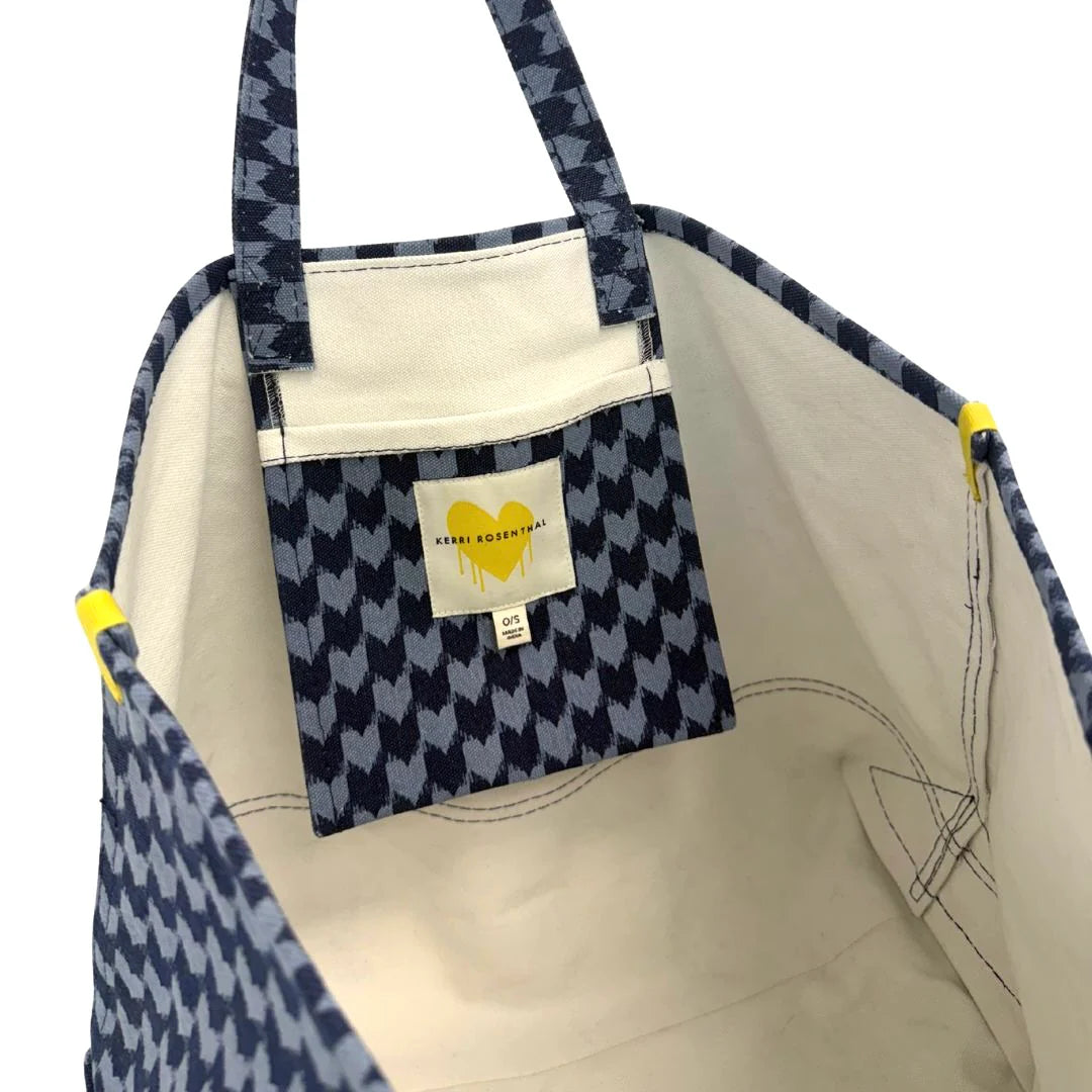 The KR Heart in Check Tote by Kerri Rosenthal features blue and white houndstooth cotton canvas, a small inner pocket with a yellow Drippy Hearts logo, a “Kerri Rosenthal” label, and cream-colored lining.