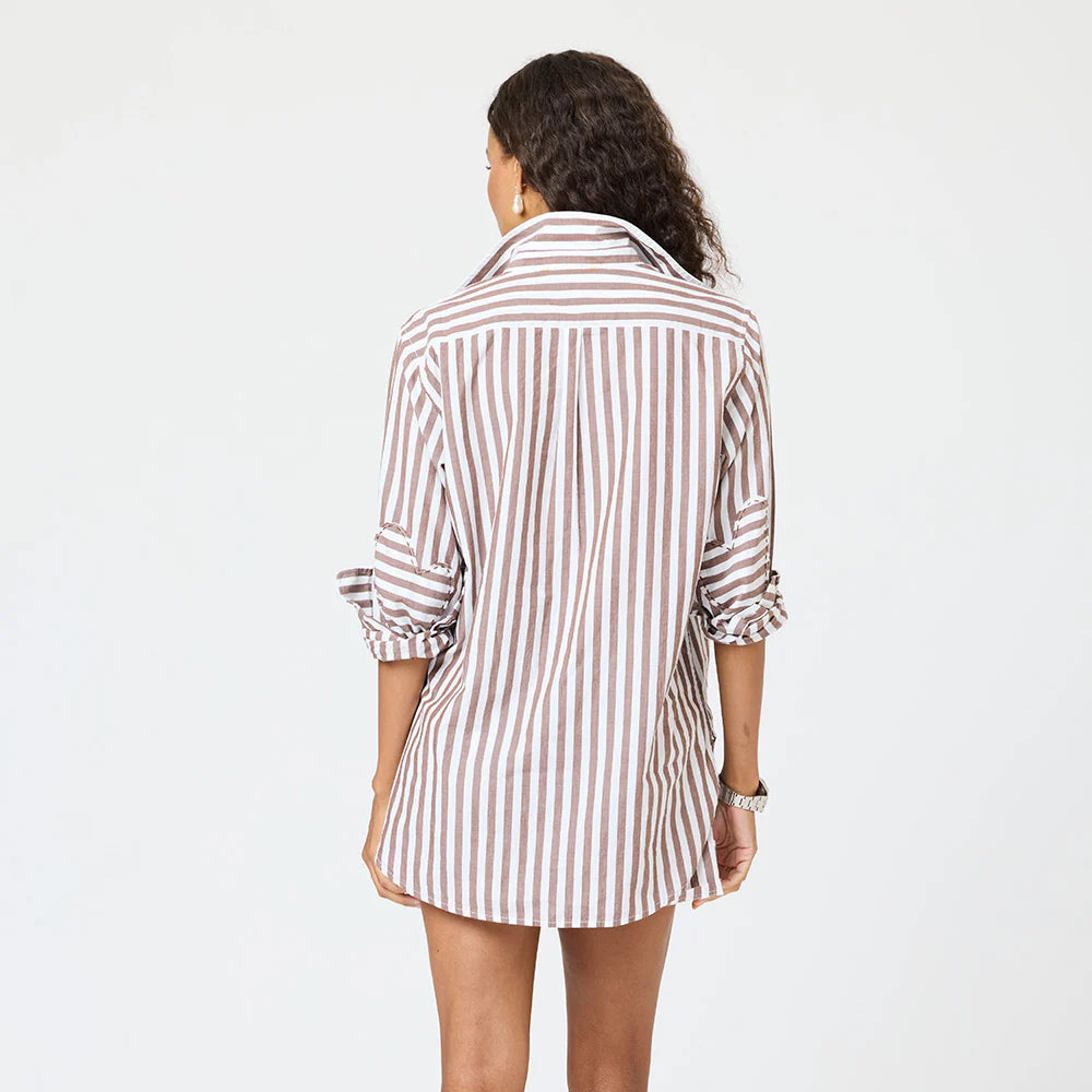 A woman with wavy hair faces away, wearing the Kerri Rosenthal Mia Stripe Shirt—long-sleeved, brown and white vertical stripes with rolled-up cuffs—posed against a plain white background.