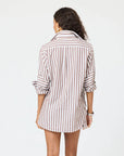 A woman with wavy hair faces away, wearing the Kerri Rosenthal Mia Stripe Shirt—long-sleeved, brown and white vertical stripes with rolled-up cuffs—posed against a plain white background.