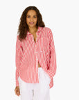 A woman with long curly hair wears the Kerri Rosenthal Mia Stripe Shirt in red and white stripes, paired with white pants, standing against a plain white background.