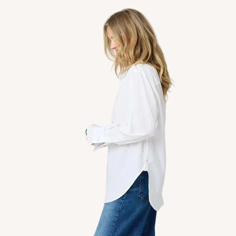 A woman with long, wavy blonde hair wears the Kerri Rosenthal Mia Ruffle Shirt and blue jeans, standing in profile against a plain light background.