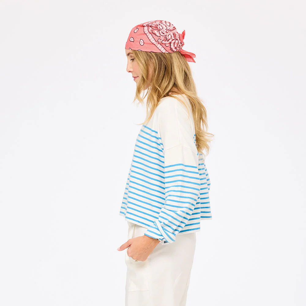 A woman with long blonde hair wears the Kerri Rosenthal Artist Long Sleeve Stripe Tee and white pants, paired with a pink bandana, standing in profile against a plain white background.