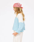 A woman with long blonde hair wears the Kerri Rosenthal Artist Long Sleeve Stripe Tee and white pants, paired with a pink bandana, standing in profile against a plain white background.