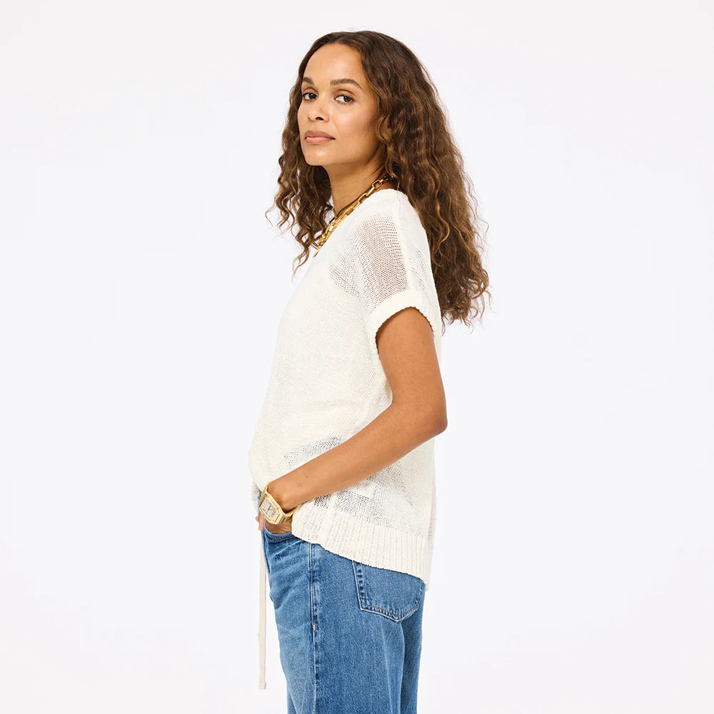 Woman with long curly hair wears the Kerri Rosenthal Summer Vestie Sweater, styled with blue jeans and gold jewelry, standing sideways with hands in her pockets against a plain white background.