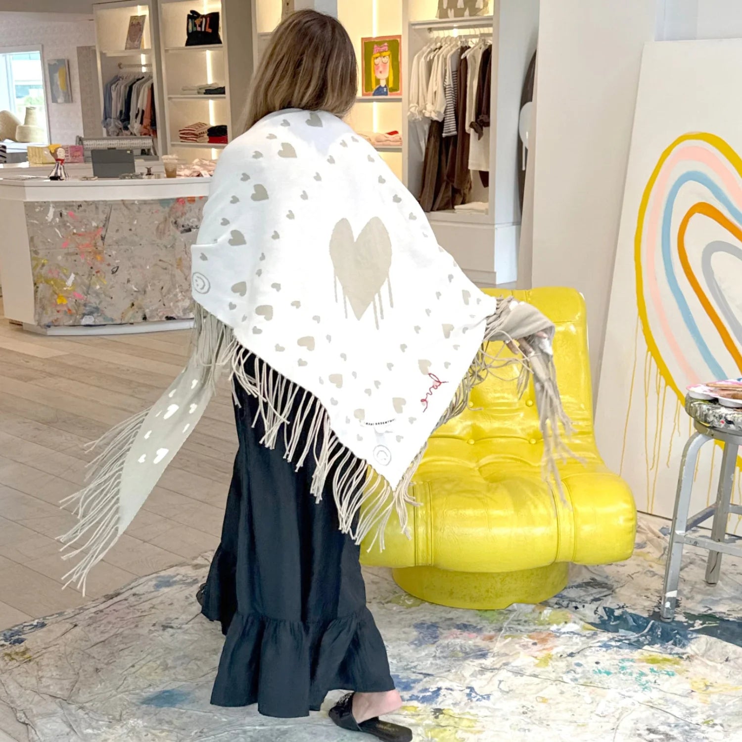 Kerri Rosenthal Imperfect Heart Poncho in black, styled in a bright boutique with yellow accent chair.