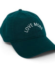 A Kerri Rosenthal Love More Hat, featuring an emerald green color and made from 100% cotton, showcases the phrase "LOVE MORE" embroidered in white text on the front panel. This baseball cap is presented on a white background.