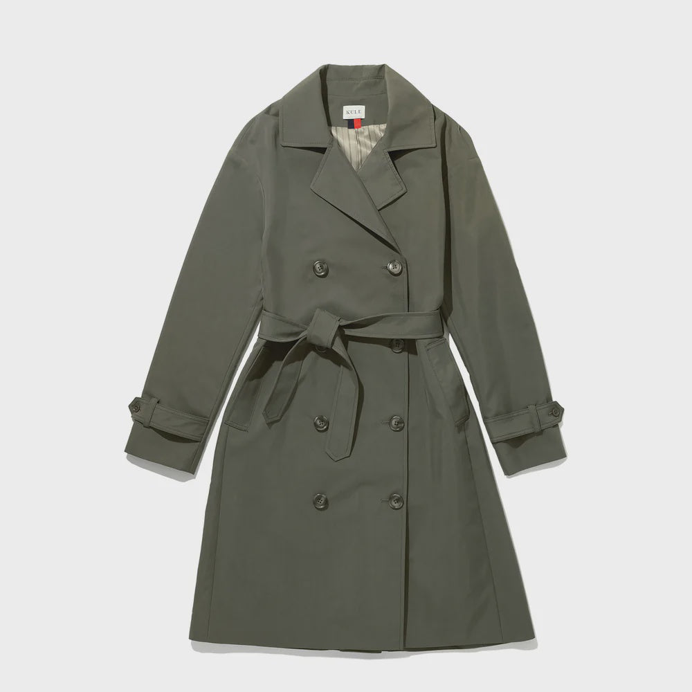Presented against a plain background, The Rox trench by Kule features a gray-green hue and an oversized fit. It showcases a double-breasted design, waist belt, and buttoned cuffs crafted from water-resistant fabric, combining style with practicality.