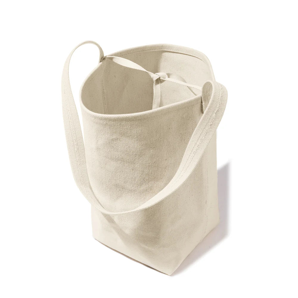 The Uma by Kule is a beige cotton canvas tote bag with long handles, shown standing upright against a white background. Its interior displays an unlined, natural fabric texture that highlights its minimalist design.