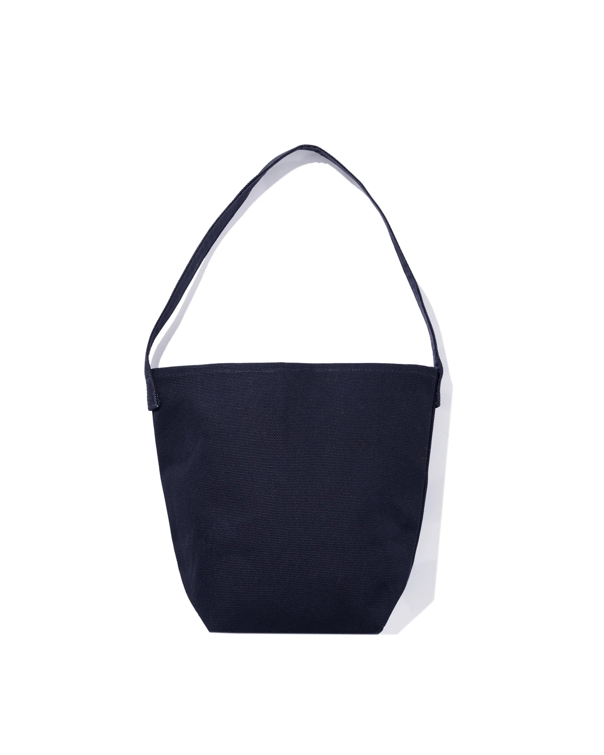 The Uma by Kule is a simple, dark navy blue cotton canvas bucket bag with a single shoulder strap, shown on a white background.