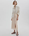 A woman poses against a plain background wearing a cream button-up shirt, Rag & Bone's kali skirt with a side slit, dark brown sandals, and her chin-length hair parted to the side.
