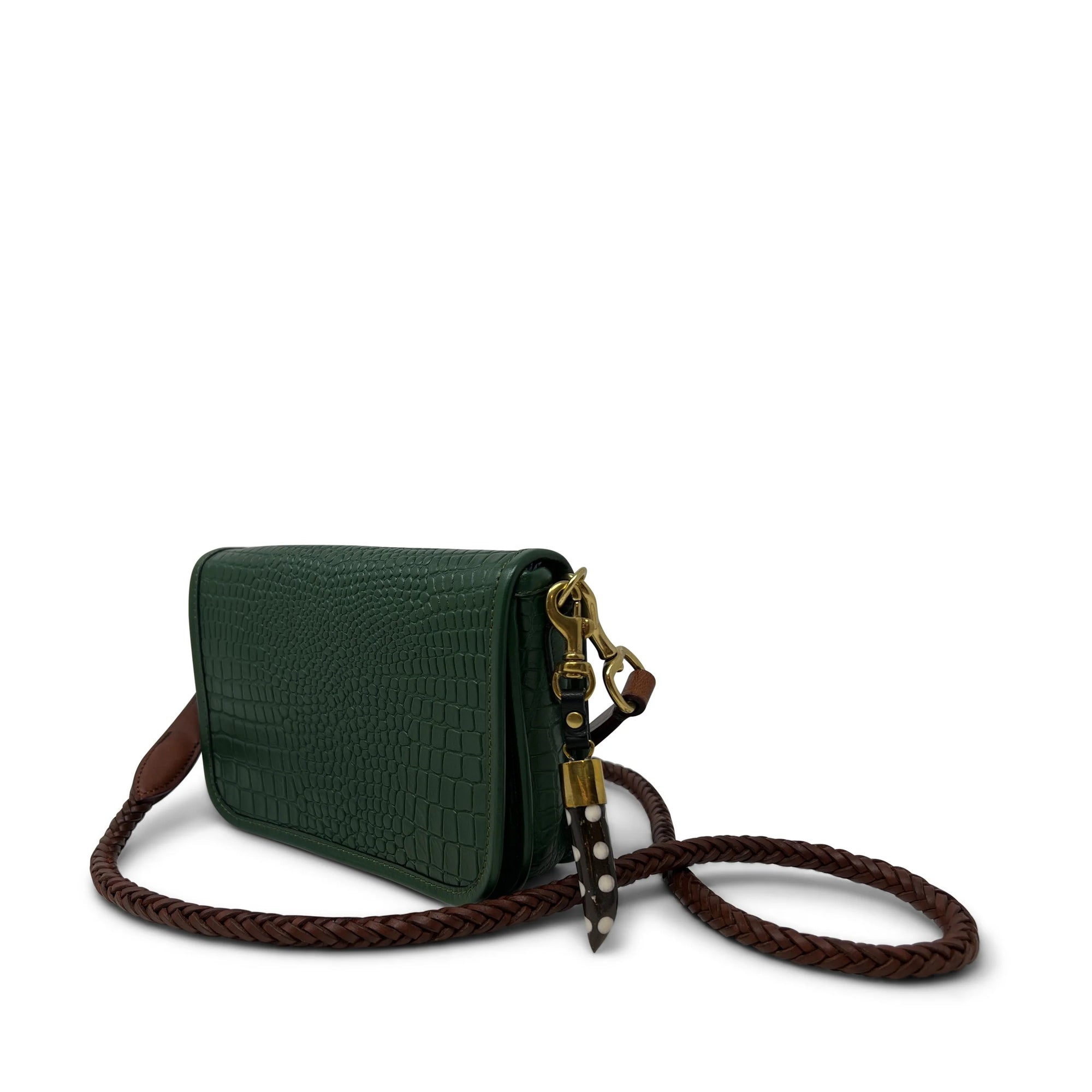 The Kempton & Co. Mini Mia Crossbody is a green, crocodile-textured compact bag with a gold clasp, brown braided strap, and black-and-white polka-dot keychain, shown against a white background.