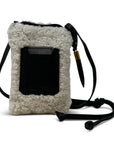 Introducing the Mini Sling Bag Natural Shearling by Kempton & Co. This compact, rectangular sling bag boasts a fluffy white shearling exterior complemented by a sleek black leather front pocket. It is designed with an adjustable leather strap featuring a decorative gold tip, perfect for showcasing your minimalistic style.