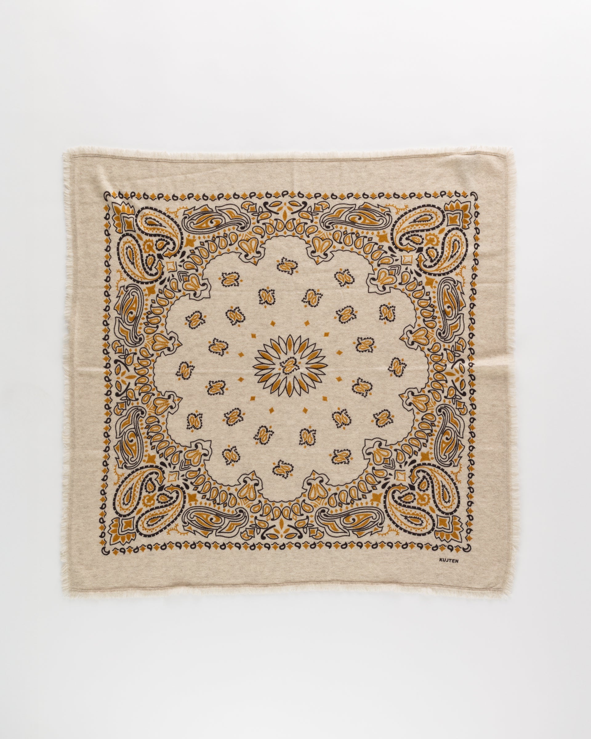 The Hachiko Scarf by Kujten is a beige square accessory made from printed jersey with frayed edges, showcasing a detailed paisley and floral pattern in yellow, brown, and black.