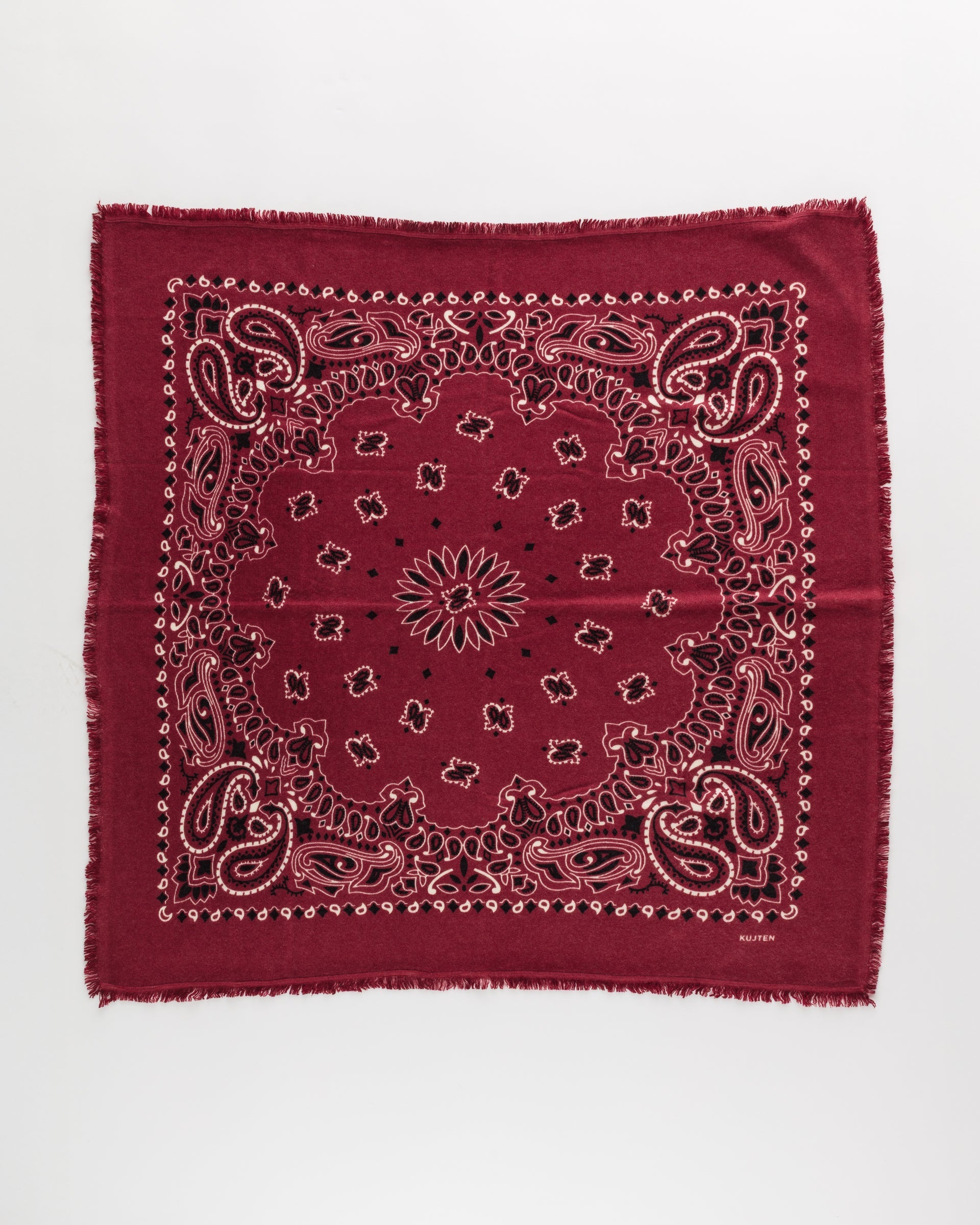 The Hachiko Scarf by BCS Group is a square maroon bandana in printed cashmere, featuring white and black paisley details with subtle frayed edges, shown flat on a white background.