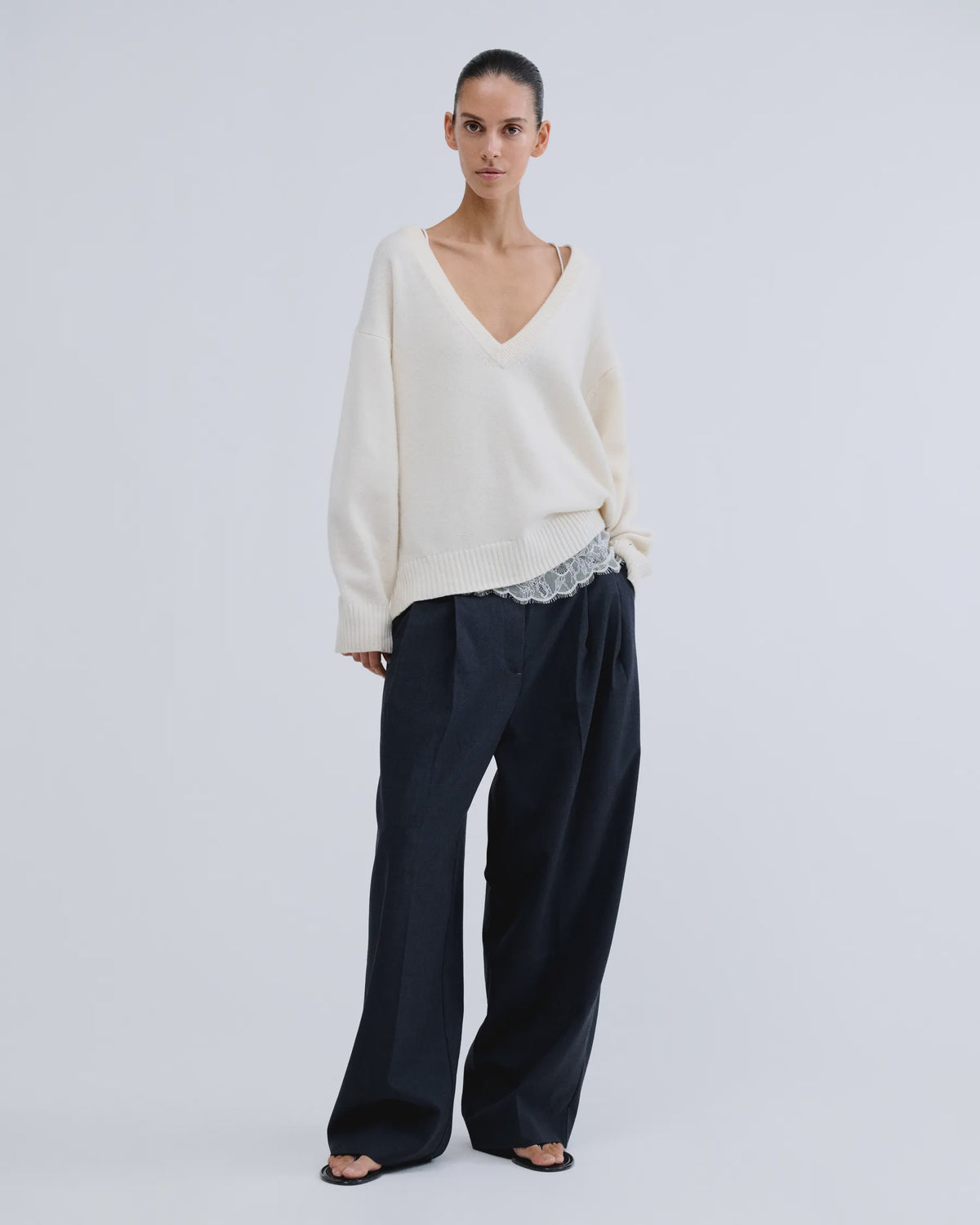 Love Stories Rachel white wool-blend V-neck jumper styled with dark wide-leg pants and sandals in a modern setting.