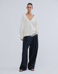 Love Stories Rachel white wool-blend V-neck jumper styled with dark wide-leg pants and sandals in a modern setting.