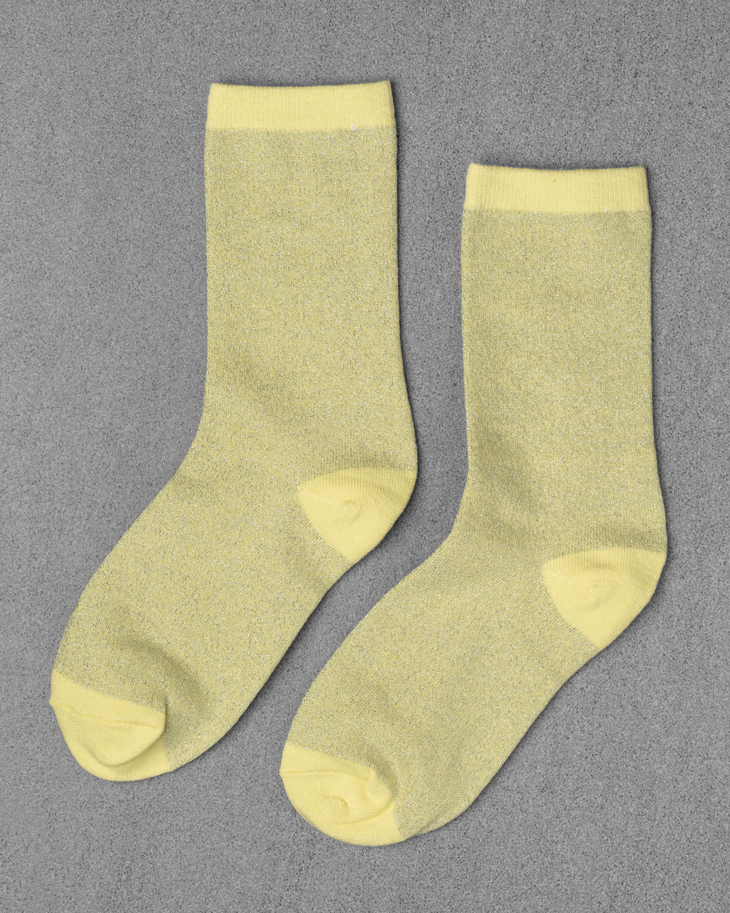 Unified Glitter Socks in light yellow with a subtle shimmer, displayed flat on a gray textured surface.
