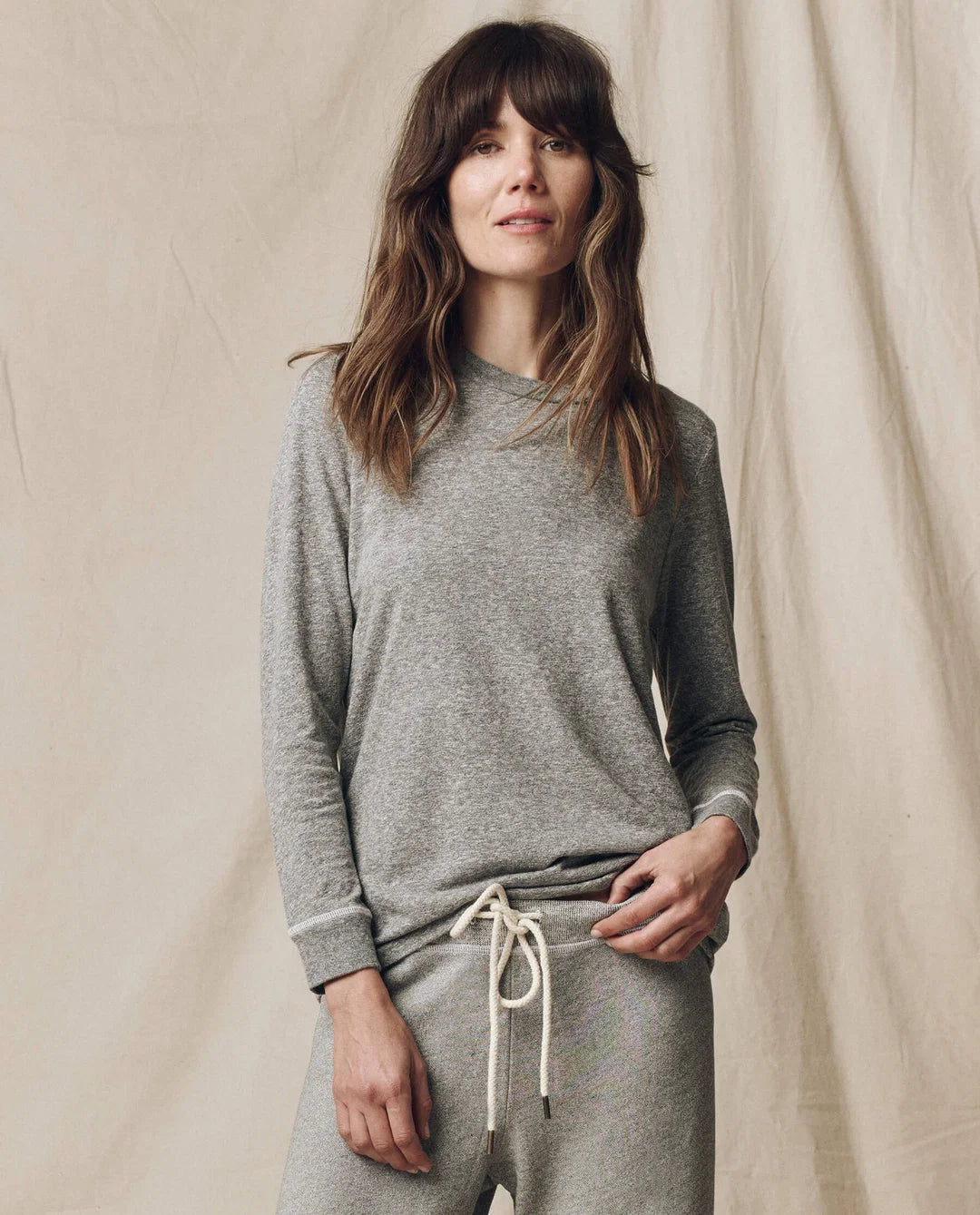 Gray Long Sleeve Slim Tee by The Great Inc. styled with sweatpants, shown against a neutral fabric backdrop.