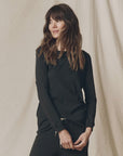 The Great Inc. Long Sleeve Slim Tee in brown, shown on a woman by a beige fabric backdrop, casual and effortless style.