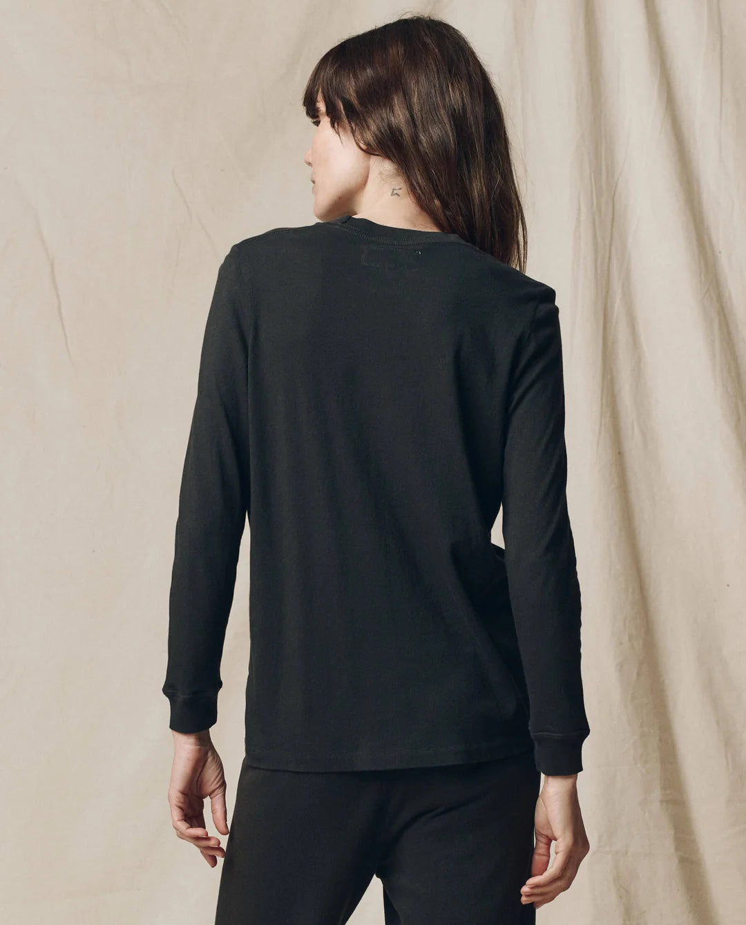 Long sleeve slim tee and pants by The Great Inc., shown from the back, against a beige fabric backdrop.