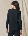 Long sleeve slim tee and pants by The Great Inc., shown from the back, against a beige fabric backdrop.