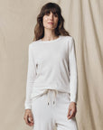 The Great Inc. Long Sleeve Slim Tee and drawstring pants in beige, worn by a smiling woman against soft backdrop.