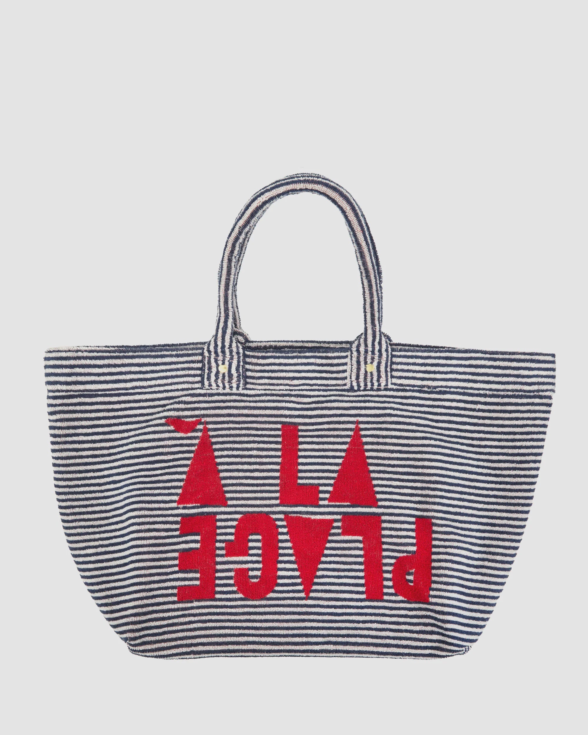 The Clare Vivier La Plage Tote is a large cotton terry cloth bag with two handles, featuring bold red “A LA PLAGE” text and shapes over black-and-white horizontal stripes on the front for a striking beach look.