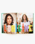 An open book features a childhood photo of a girl on the left and a grown woman at her desk on the right, radiating Paris Chic/L.A. Cool. The vibrant text across the pages reads "La Vie De Clare V.", reflecting Clare Vivier's style as fashion inspiration.