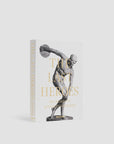 Assouline presents "The Last Heroes: 100 Moments of Olympics Legend," a hardcover book that features a striking black-and-white image of a classical Greek statue of an athlete, possibly a discus thrower, in mid-action on a white background. This essential volume is perfect for fans of Summer Olympics history as we approach the Paris 2024 Olympics.