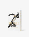 The image features an Assouline book titled "The Last Heroes: 100 Moments of Olympics Legend," with a black and white photo of an athlete in mid-sprint on the cover. The book, which delves into Summer Olympics history, is positioned standing upright, displaying both the front cover and spine.