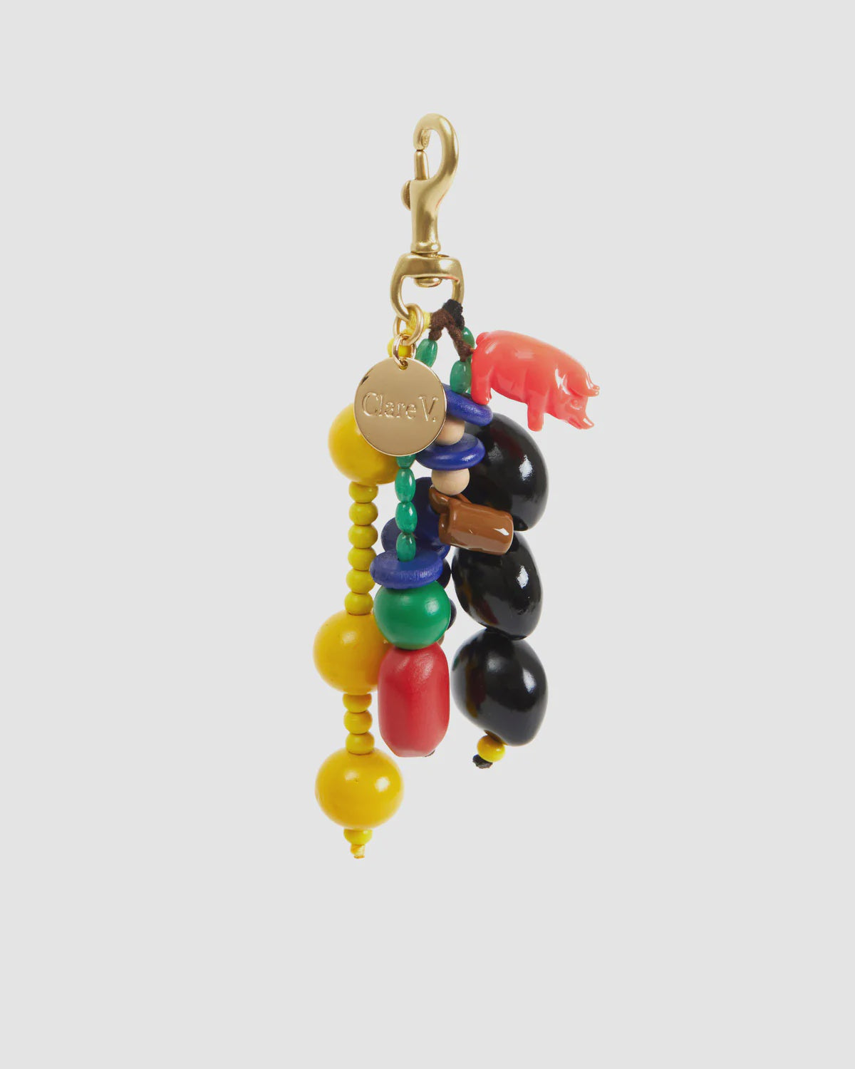 The Le Long Beaded Tassel by Clare Vivier is a colorful keychain featuring wood beads in yellow, red, black, and blue with a small pink rhinoceros charm. It includes a vintage gold-plated tag and is attached to a beaded fob secured by a gold clasp.